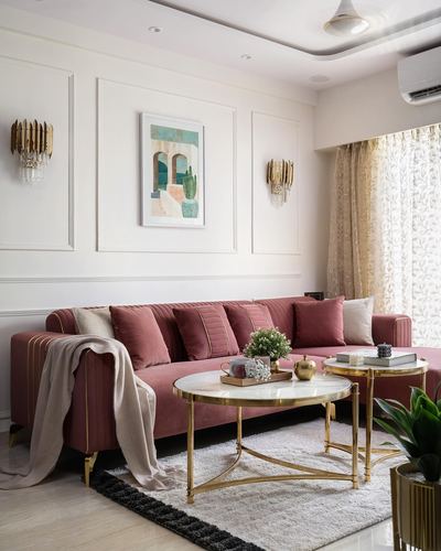 Pink velvet sectional sofa with gold trim beneath framed art and brass wall sconces