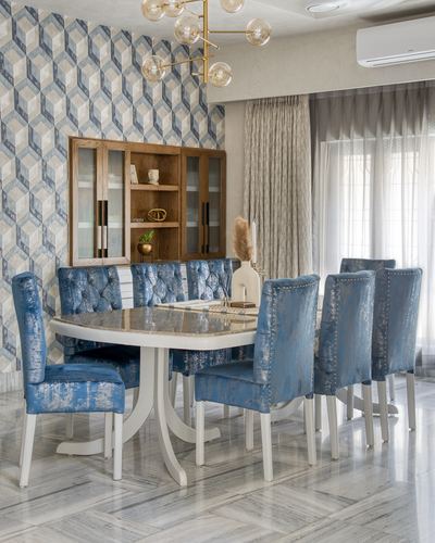 Dining room with round marble table, blue tufted chairs, wooden display cabinet against geometric wallpaper