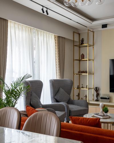 Living room corner with houndstooth wingback chairs, orange sofa, and gold étagère shelving near sheer curtains