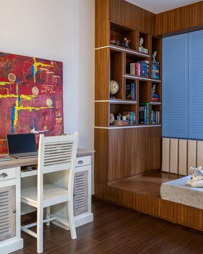 Study desk with laptop beside wooden cubby bookshelf and raised platform bed with blue shutters