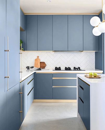 Blue matte kitchen cabinetry with brass trim, white herringbone backsplash and stone island.