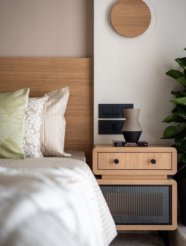 Wood headboard and rounded nightstand with lamp and books beside a round wood mirror