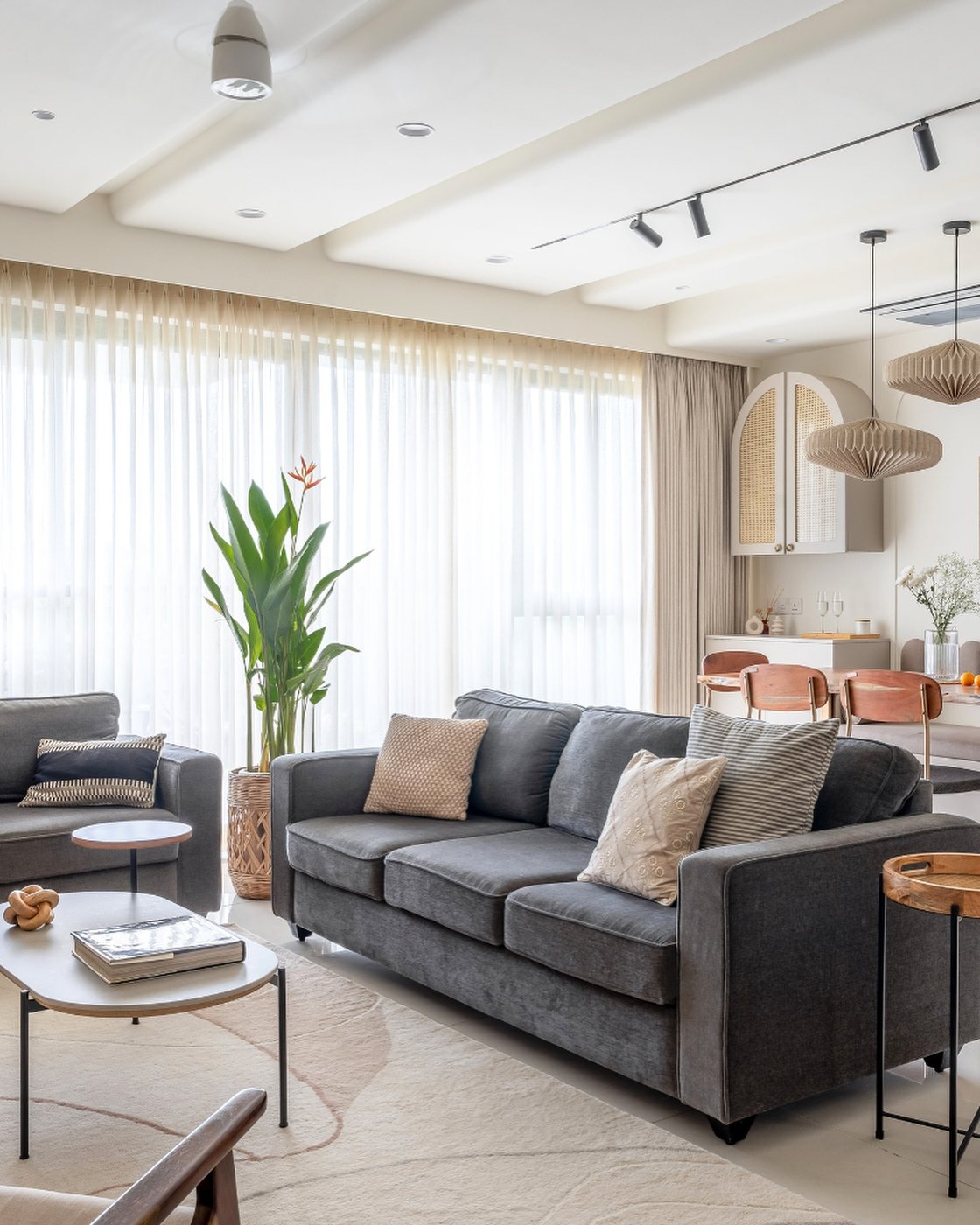 Grey sofas around rounded coffee tables in a sunlit living room with sheer floor-to-ceiling curtains