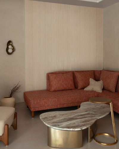 Terracotta sectional sofa against fluted cream wall with sculptural marble coffee table on brass base