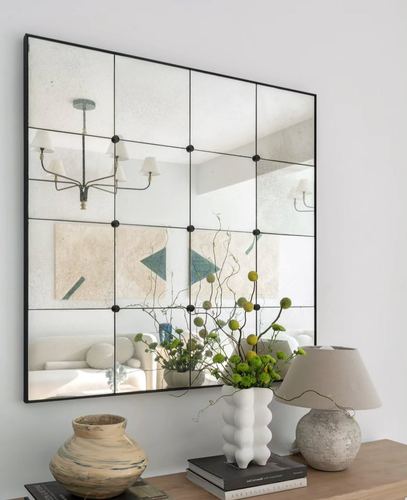 Console vignette with gridded mirror reflecting living room, vases and lamp on wood surface