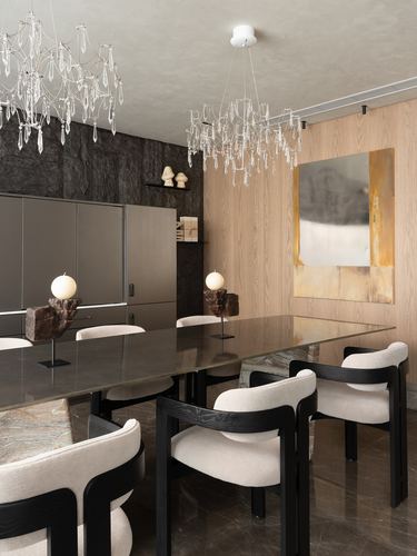 Dining room with marble table, black and cream chairs, two crystal chandeliers, stone and wood feature walls