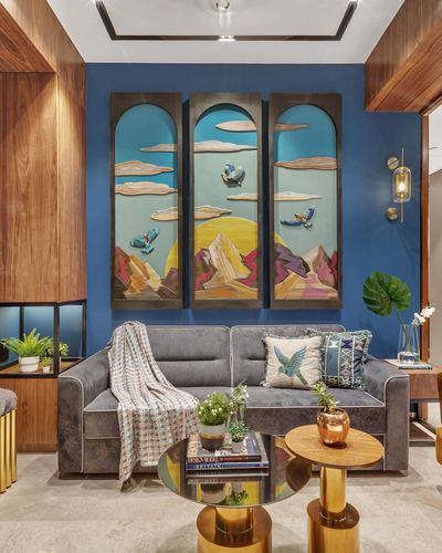 Living room with blue wall, arched triptych art, grey tufted sofa and brass side tables