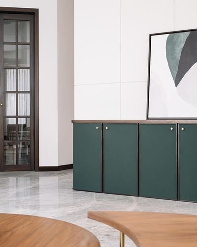 Green paneled cabinetry beneath abstract art beside a glazed wood door on marble floor