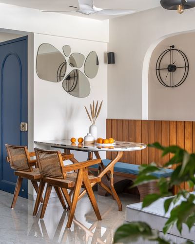 Dining nook with cane armchairs, marble-pattern table, slatted wood bench and organic mirror cluster on wall