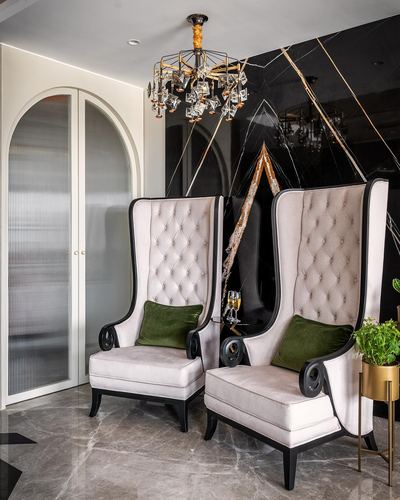Two tall tufted wingback chairs before a black patterned wall with a crystal chandelier above