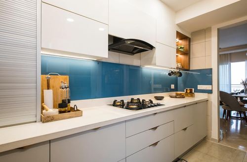 Modern white kitchen with teal glass backsplash, black hob, and glossy cabinetry