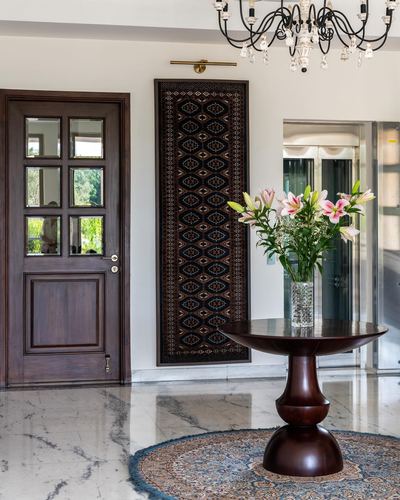 Foyer with wood door, framed textile panel, marble floor, round wood table with lilies