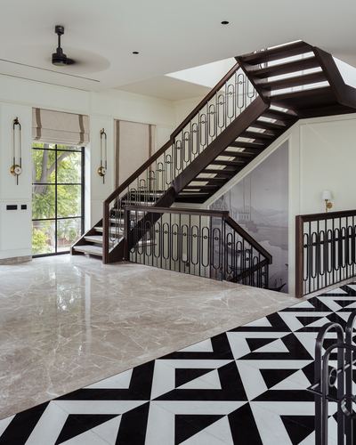 Double-height foyer with dark wood staircase, iron balustrade, and black-and-white geometric floor tiles