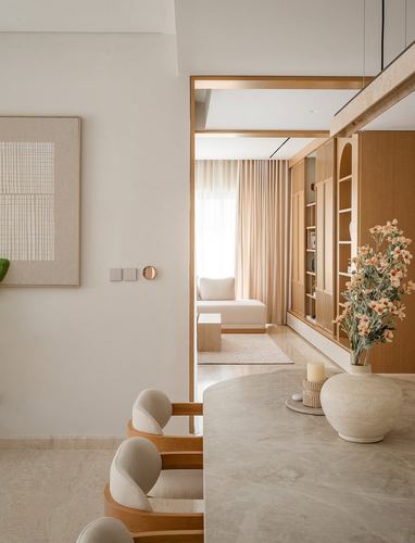 Beige stone dining table foreground with view through wood-framed archway to a living room with curtains and shelving.
