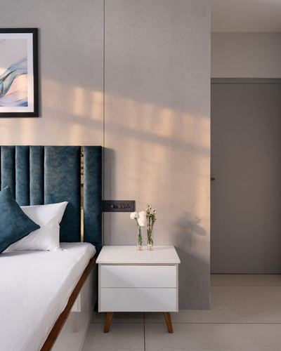 Bedside vignette with teal tufted headboard, white nightstand, and dappled afternoon light on wall