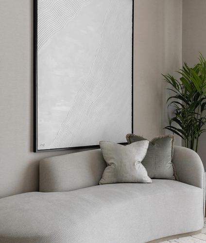 Curved grey upholstered sofa with textured pillows beneath a framed abstract wave artwork, plant beside it