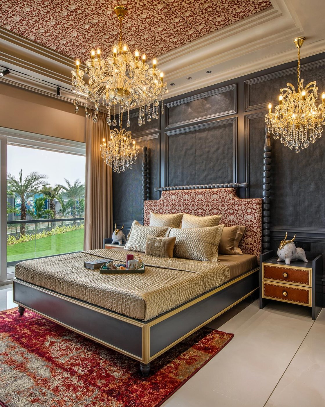Luxurious bedroom with dark paneled wall, red tufted headboard, gold bedding and crystal chandeliers