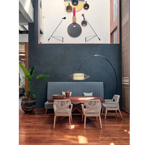 Dining nook with wood table, woven chairs, grey banquette and oversized arc lamp under double-height wall