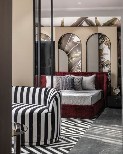Bedroom with red velvet bed, arched leaf-patterned panels, striped chair, chevron floor