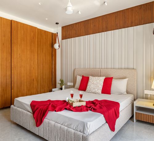 Bedroom with wood wardrobe, ribbed wall panel, and red throw with wine glasses on bed