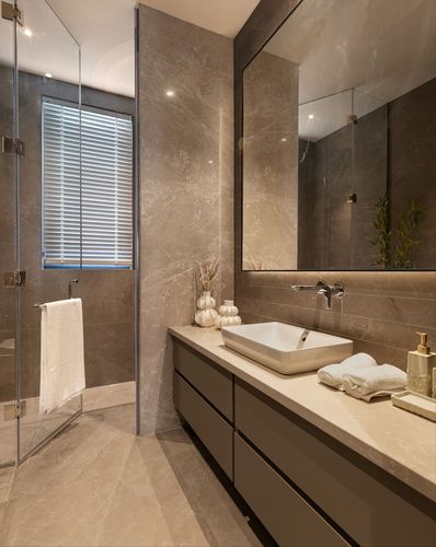 Beige stone bathroom with vessel sink, wall-mounted faucet, and glass shower enclosure