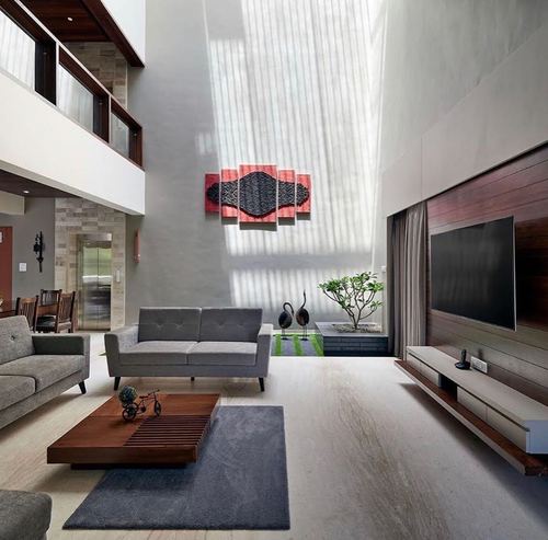 Double-height living room with sheer curtains, grey sofas, wooden coffee table and wall-mounted tv unit