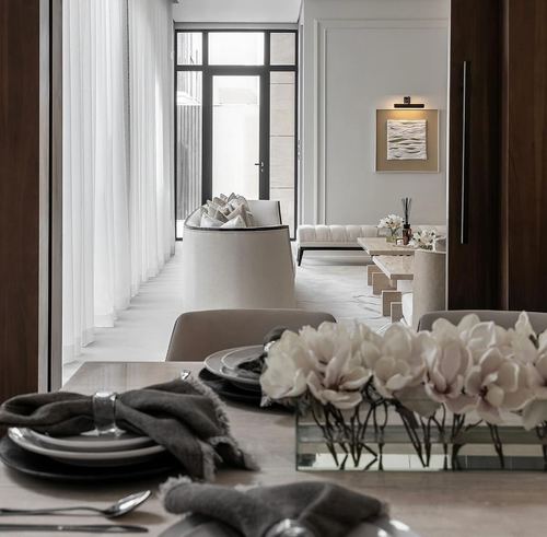 Dining table set with grey linens and white blooms, view through to living room and glass door beyond