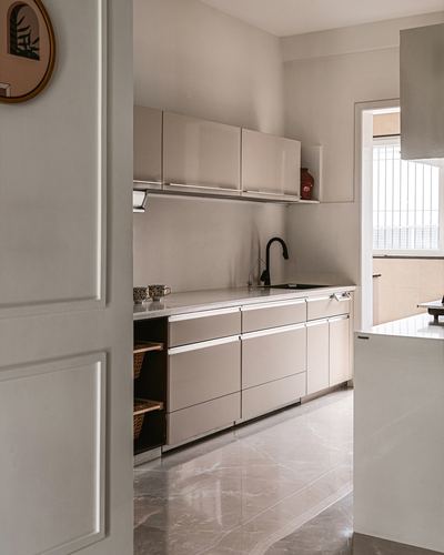 View through a white paneled doorway into a beige galley kitchen with stone flooring
