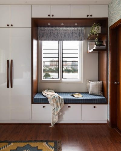 Window seat nook with blue checkered cushion, throw blanket, and city view through window