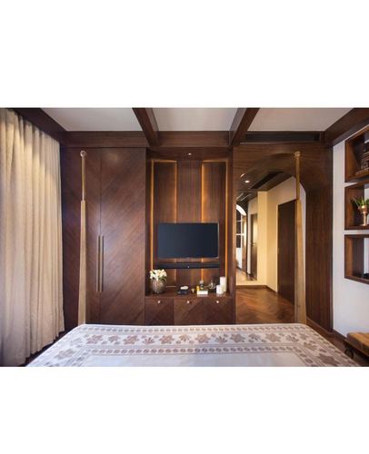 Wood-paneled bedroom with brass four-poster bed, built-in TV unit, and herringbone flooring