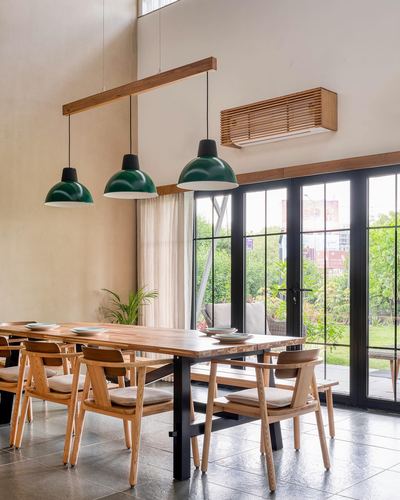 Dining table with wooden chairs under three green pendant lights beside black-framed glass doors