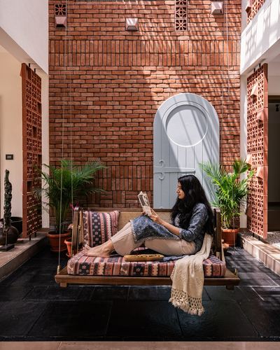Woman reading on a cane-backed swing in a brick courtyard with an arched blue door