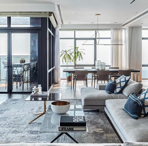 Contemporary living room with grey sectional, marble coffee table, and dining area framed by floor-to-ceiling windows
