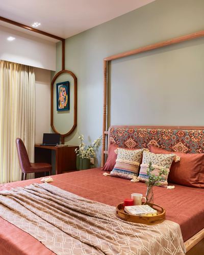 Bedroom with terracotta bedding, wooden canopy headboard, sage green walls, and oval mirror