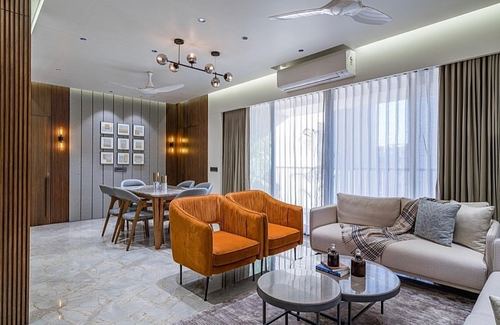Open living and dining room with orange velvet armchairs, beige sofa, and marble floor