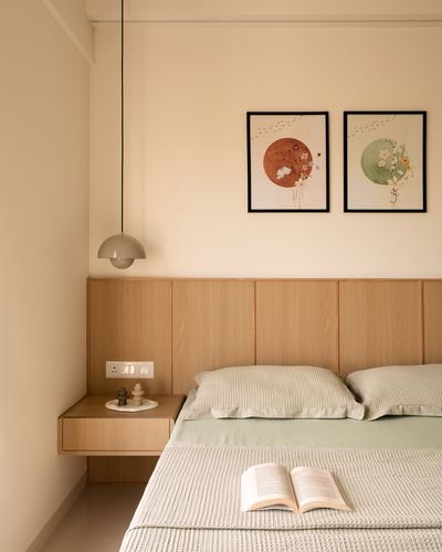 Bedroom corner with wood panel headboard wall, floating nightstand, pendant light, and two framed botanical prints above.