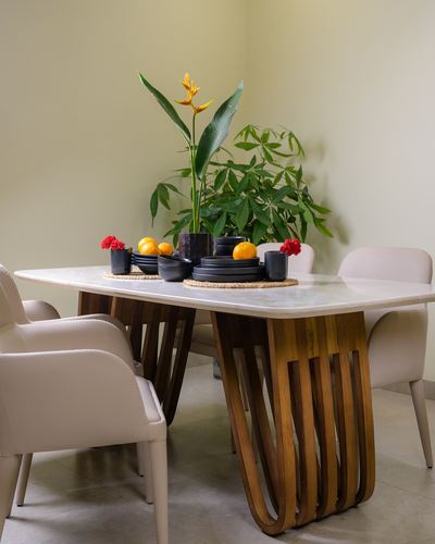 Marble-top dining table with sculpted wooden slat legs, set with black dinnerware and a bird of paradise centerpiece