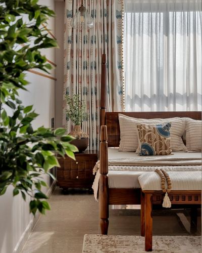 Wooden four-poster bed with patterned pillows beside sheer curtained window and indoor plants