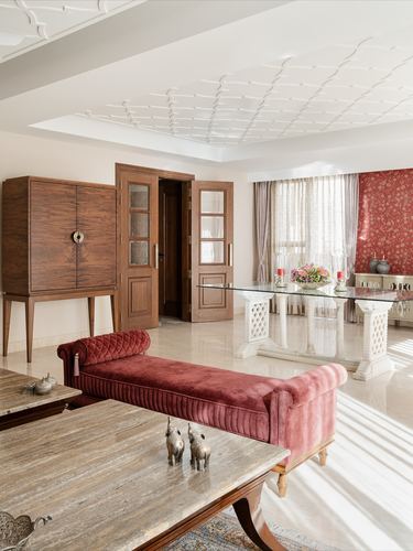 Living room with marble floor, carved wood cabinet, red velvet daybed, and glass dining table