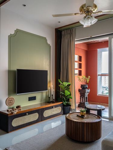 Living room with arched sage green tv wall, cane-front console, round wood coffee table, and terracotta balcony beyond