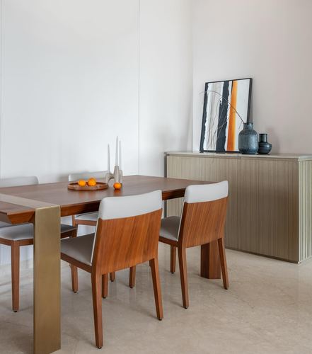 Dining table with wood chairs, brass leg detail, and sideboard with artwork against beige walls