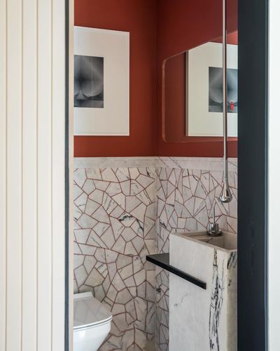 Small bathroom with terracotta walls, cracked marble mosaic tiling, framed photo, and marble pedestal sink seen through a doorway.