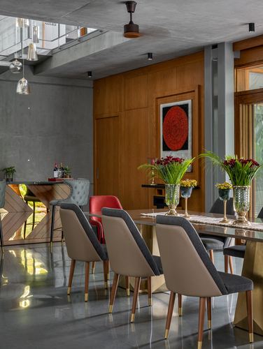 Dining area with grey and tan chairs, wood paneled wall, red circular art, concrete ceiling
