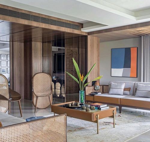 Living room with cane chairs, tan leather sofa, wood paneling and abstract art