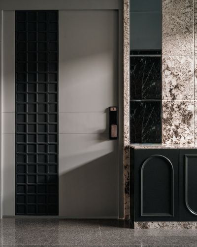 Entry door with waffle-textured black panel beside stone-clad wall and dark arched cabinetry