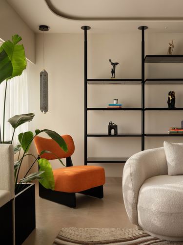 Living room corner with orange chair, black open shelving, and cream curved sofa