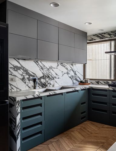 Modern kitchen with grey upper cabinets, veined stone backsplash and dark green lower cabinets on herringbone wood floor