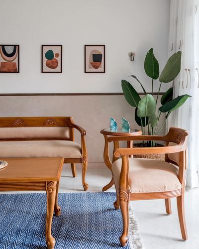 Living room with carved wooden bench, armchair, indigo rug and large leafy plant near arched doorway