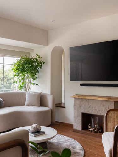 Living room with curved beige sofa, stone fireplace, wall tv, arched window seat, indoor plant