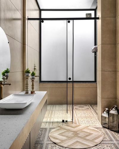Bathroom with beige stone walls, patterned tile floor, vessel sink, and frosted glass shower partition under skylight